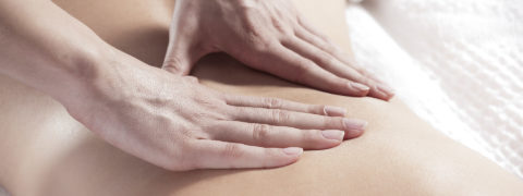 a close up shot of a woman's bare back. A pair of hands is massaging the middle of the woman's back.