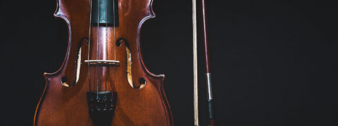 a dark wood violin and red bow are positionedin front of a black background