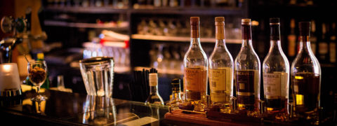 Detail shot of a bar. There are five bottles of whiskey lined up on the bar each with its own unique label.