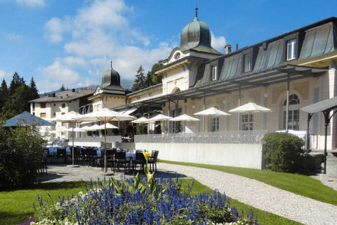 beautiful shot of the Belle Époque pavilion with outdoor seating area, cafe tables and chairs, sun umbrellas, trees, grass and blooming flowers