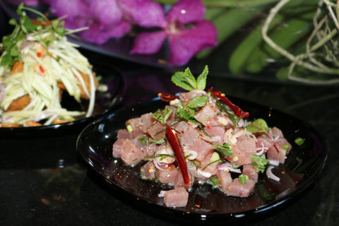 a detail shot of a dish of sashimi. Their is a large helping of raw fish garnished with red peppers and green mint leaves.