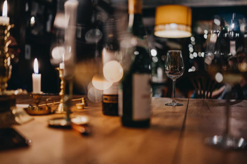 detail shot of a wine tasting. There are multiple bottles of wine on a wooden table. There are wine glasses and gold candle sticks placed around the table.
