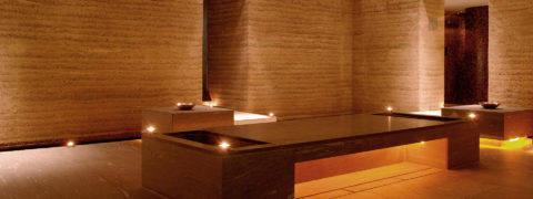 a golden tinted room with a long bench in the center of it. he walls are textured and light brown. There are lights that give the room a golden glow.