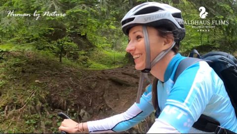 woman smiling while riding a bike and wearing a backpack, helmet and biking gear