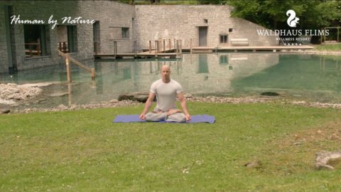 man on a yoga mat meditating next to Waldhaus Flims outdoor pond