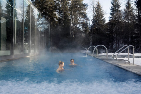 a couple in the steamy outdoor pool surrounded by trees and blue sky