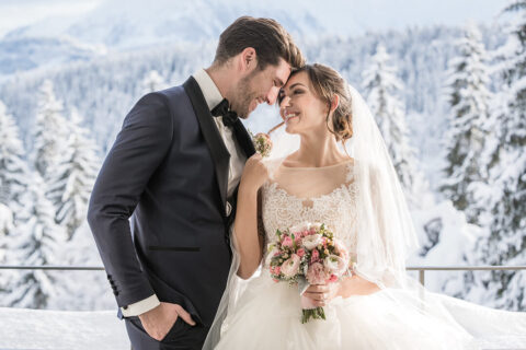 winter wedding, groom and bride being close together and looking at each other, with snow covered trees and mountains as the backdrop