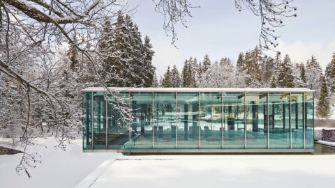 beautiful winter scene of the Waldhaus Spa glass building, white snow on the ground and surrounding trees, clear blue sky in the background
