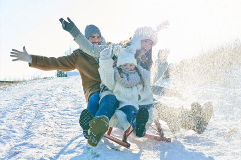 A young family enjoys sledding during a winter holiday in the Swiss Alps at Waldhaus Flims Wellness Resort & Spa